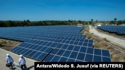 Dua petugas Perusahaan Listrik Negara (PLN) melintasi panel sel surya di pembangkit listrik tenaga surya terbesar di Desa Oelpuah, Kupang, 20 Juli 2017. (Foto: Antara/Widodo S. Jusuf via Reuters)