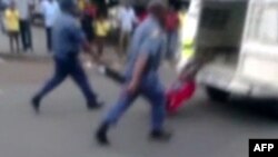 Bức ảnh trích từ một video nghiệp dư được đăng trên nhật báo South African Daily Sun cho thấy cảnh sát nắm chân của người tài xế taxi bị còng vào phía sau chiếc xe