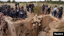 Warga masyarakat menyaksikan Menteri Kepolisian Afrika Selatan, Senzo Mchunu, memeriksa bagian luar terowongan tambang tempat ratusan penambang ilegal diperkirakan bersembunyi di bawah tanah, di Stilfontein, Afrika Selatan, 15 November 2024. (Ihsaan Haffejee/REUTERS)